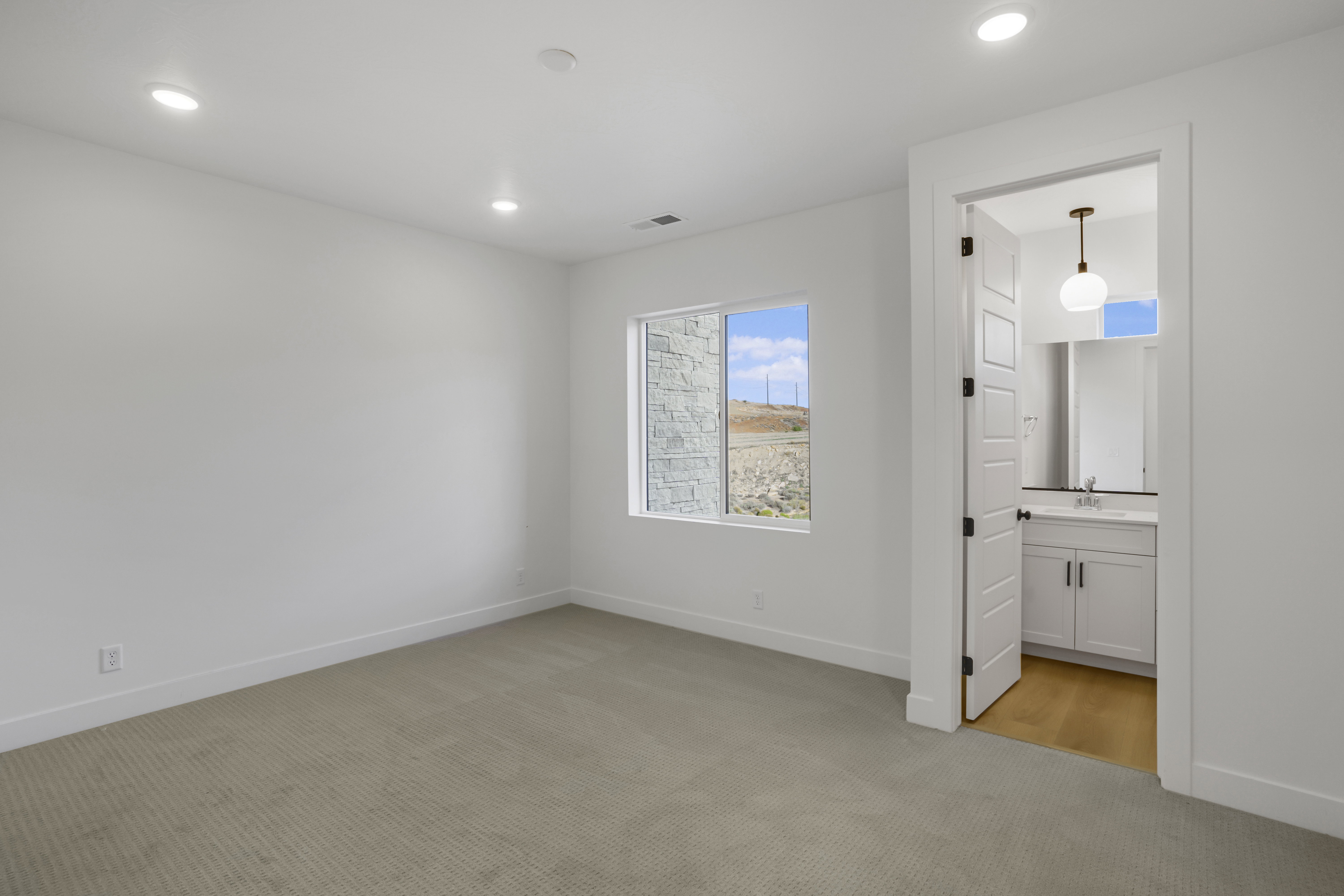 Neutral wall color with recessed lighting, light-toned carpeting, and a window with a stone exterior visible