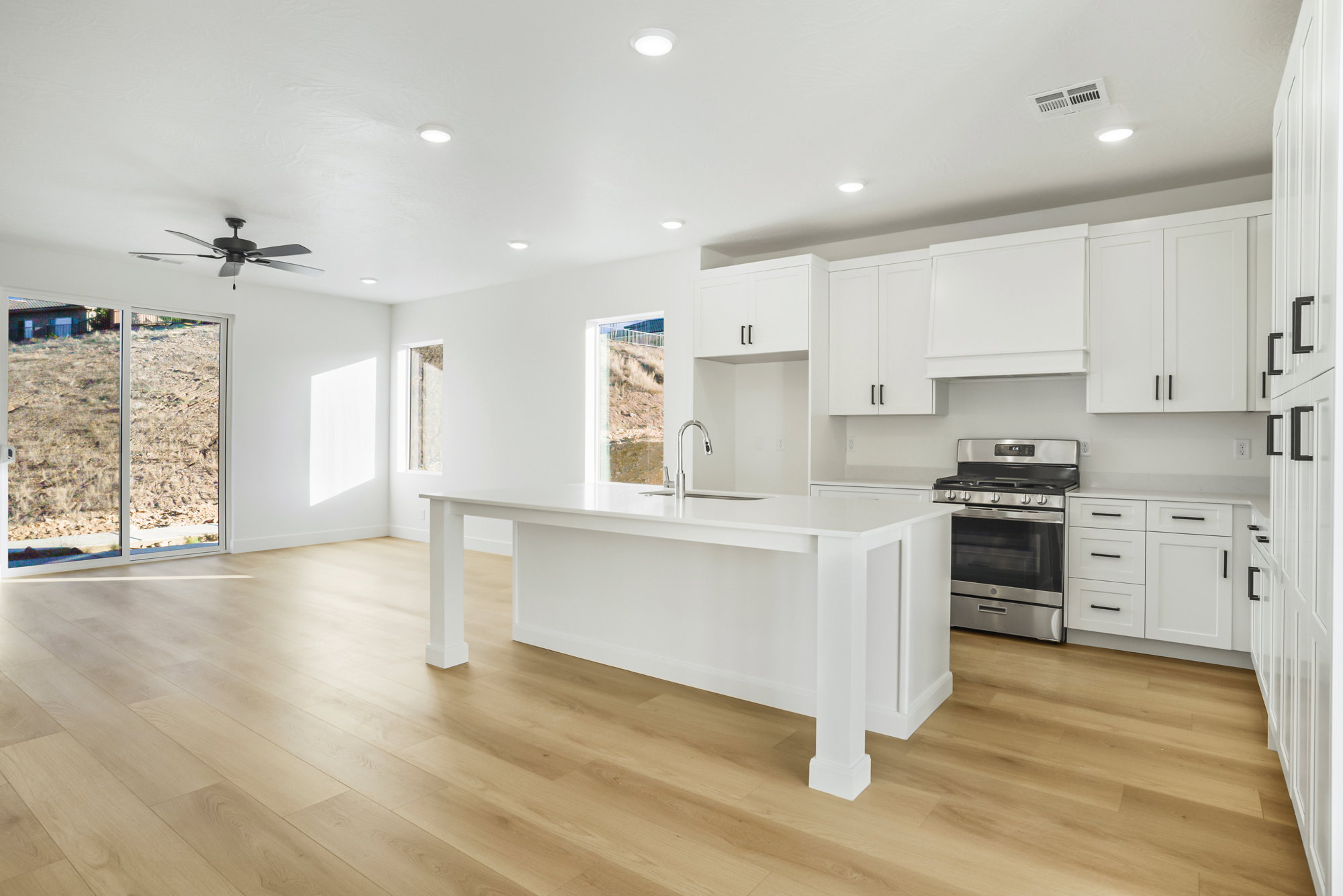 Open-concept kitchen and living area featuring light wood-finish flooring, white cabinetry, a central island with a sink, a stainless steel range, and recessed lighting
