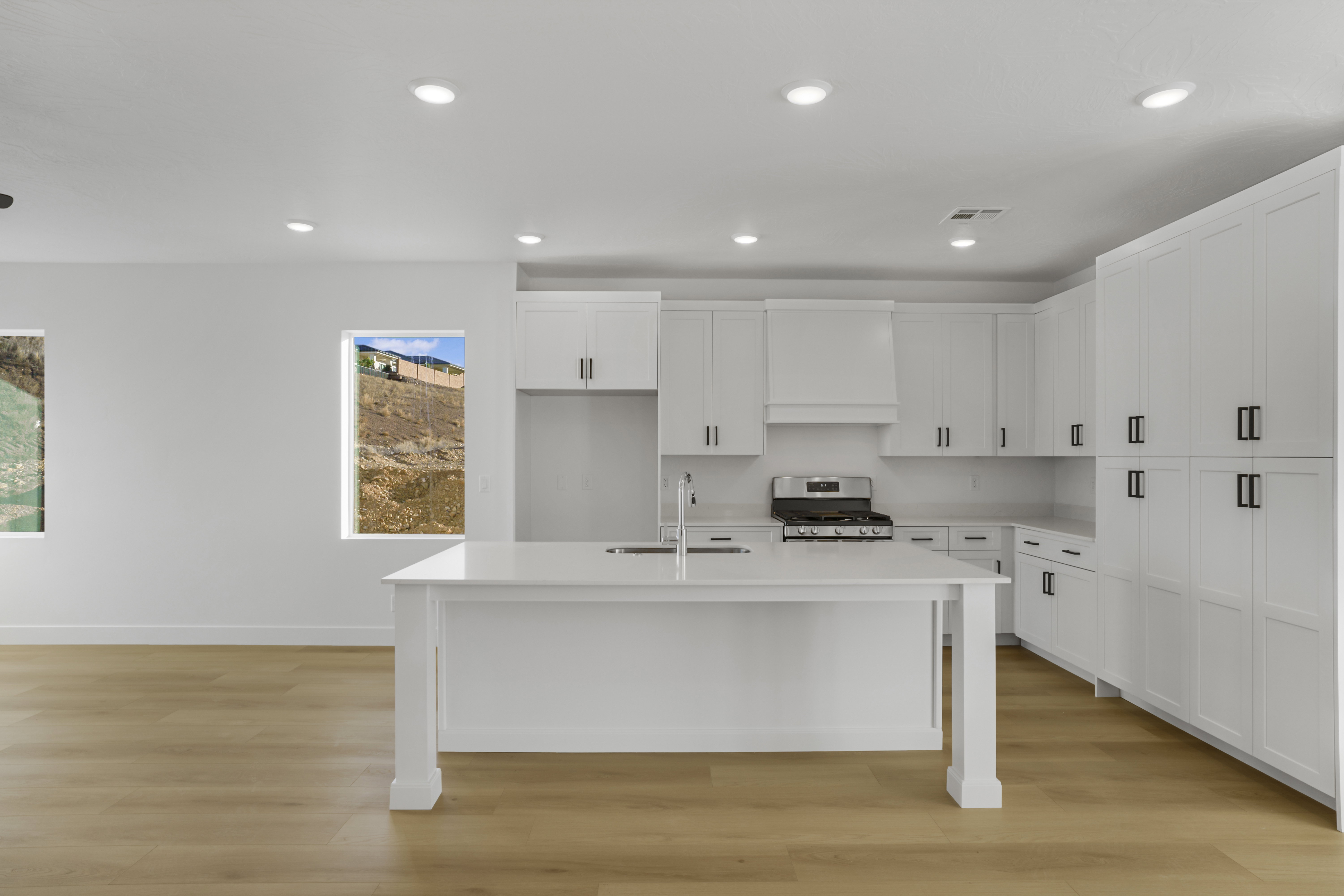 Modern kitchen featuring a large central island with an integrated sink, white cabinetry, stainless steel range, and light wood-finish flooring