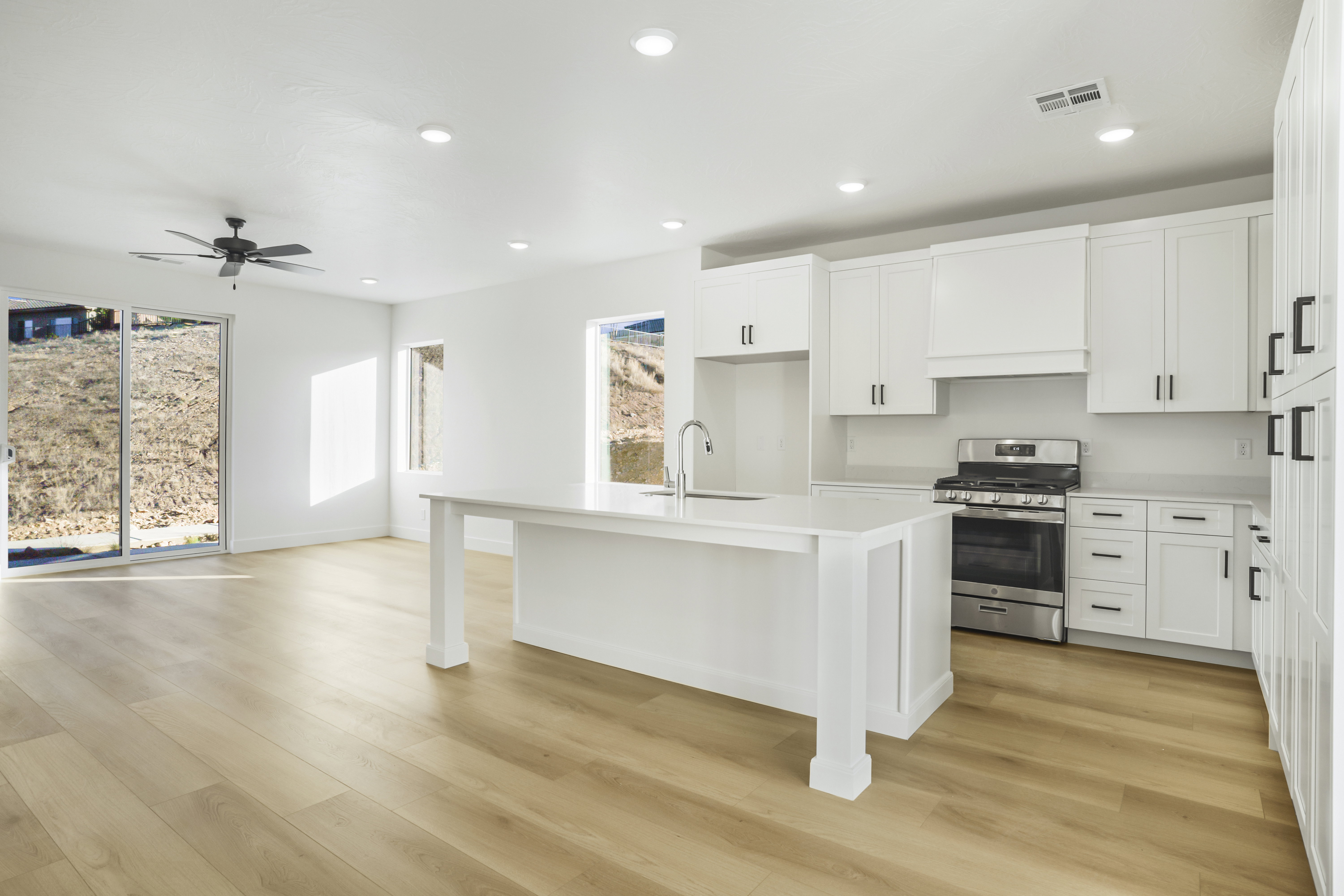 Open-concept living area with light wood-finish flooring, recessed lighting, and a dark ceiling fan