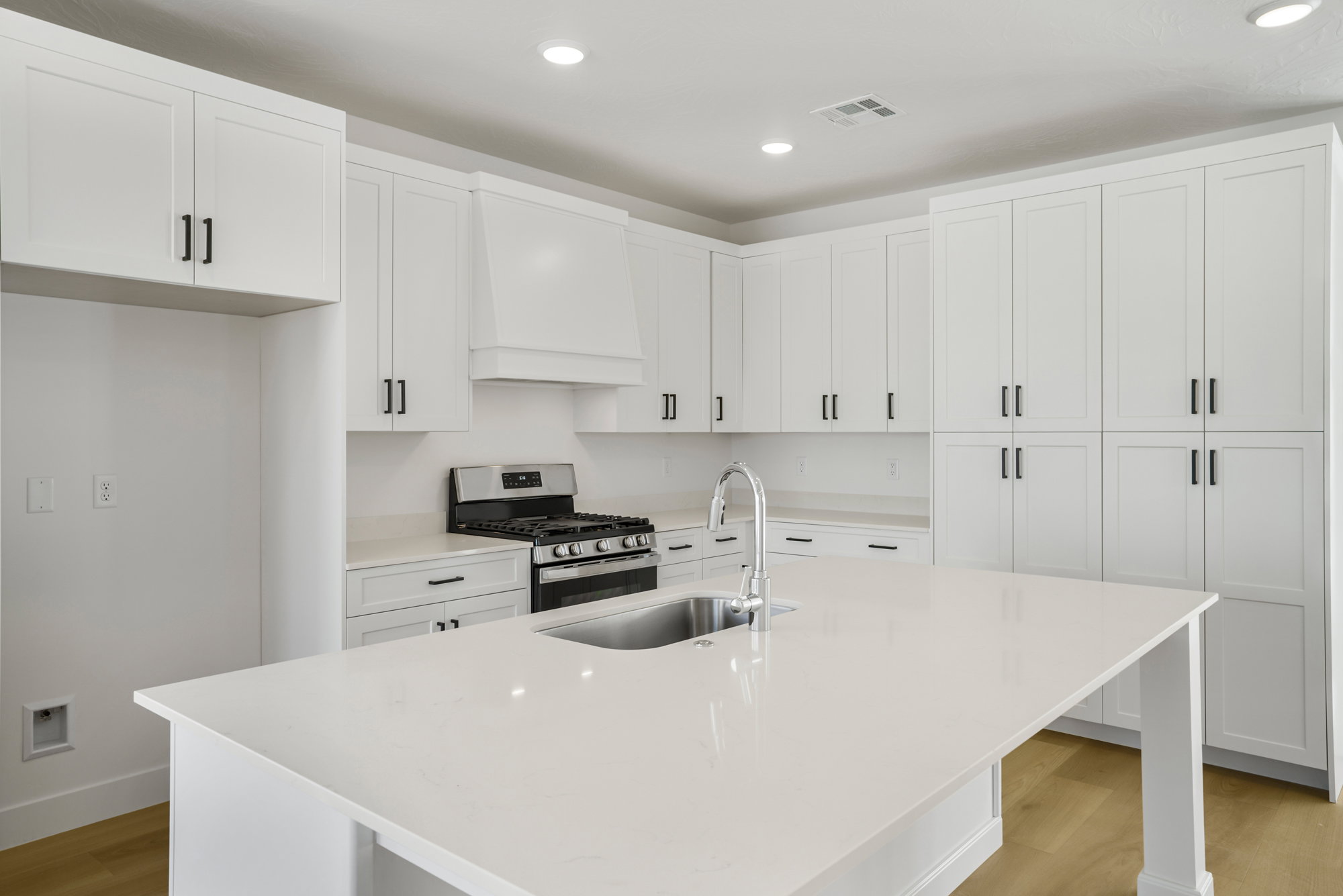Kitchen featuring a central island with an undermount sink and gooseneck faucet, extensive white cabinetry with matte black hardware, light-toned countertops, and recessed lighting
