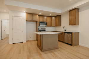 Kitchen featuring brown cabinetry, appliances with stainless steel finishes, a kitchen island, recessed lighting, and light wood-type flooring