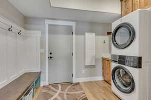 Laundry room featuring cabinet space, stacked washer / dryer, and light wood-style flooring