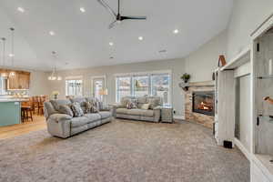 Living room with a glass covered fireplace, a ceiling fan, recessed lighting, high vaulted ceiling, and light colored carpet