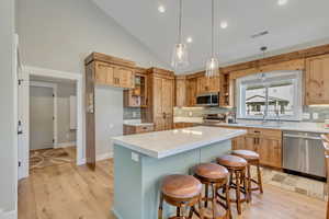 Kitchen featuring hanging light fixtures, appliances with stainless steel finishes, light wood-style flooring, a breakfast bar, and high vaulted ceiling