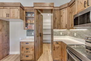 Kitchen with appliances with stainless steel finishes, light stone countertops, light wood-style flooring, backsplash, and glass insert cabinets