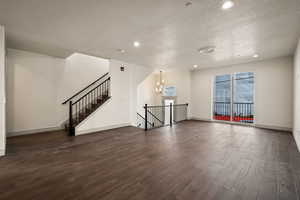 Unfurnished living room featuring a chandelier, a textured ceiling, recessed lighting, and dark wood-type flooring