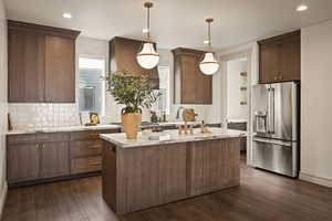 Kitchen with high quality fridge, dark wood-type flooring, pendant lighting, an island with sink, and exhaust hood