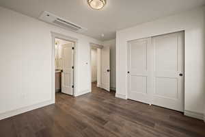 Unfurnished bedroom with dark wood-type flooring, a closet, connected bathroom, and a textured ceiling