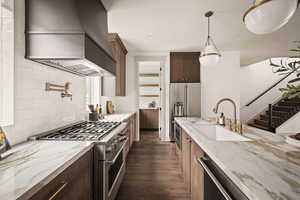 Kitchen featuring appliances with stainless steel finishes, light stone countertops, custom range hood, and hanging light fixtures