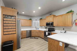 Kitchen featuring stainless steel appliances, recessed lighting, light stone countertops, a peninsula, and light wood-type flooring