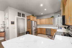 Kitchen with stainless steel appliances, light stone counters, light brown cabinets, and recessed lighting