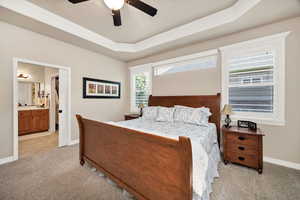 Bedroom with light colored carpet, a ceiling fan, ensuite bath, ornamental molding, and a raised ceiling
