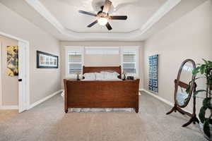 Bedroom with carpet flooring, a ceiling fan, a tray ceiling, and multiple windows