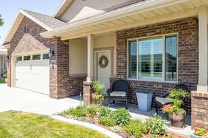 Property entrance with a porch, brick siding, a shingled roof, an attached garage, and concrete driveway