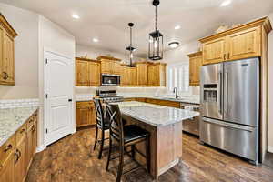 Kitchen featuring appliances with stainless steel finishes, light stone counters, pendant lighting, a kitchen bar, and a center island