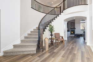 Staircase with a high ceiling, wood finished floors, arched walkways, and a glass covered fireplace