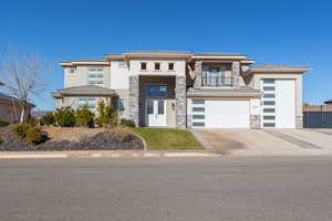 Prairie-style house with concrete driveway, stucco siding, stone siding, a balcony, and an attached garage