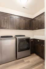 Washroom with cabinet space, light wood-type flooring, and washer and dryer