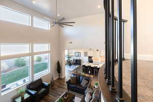 Living room with healthy amount of natural light, ceiling fan, recessed lighting, dark wood-style floors, and a high ceiling