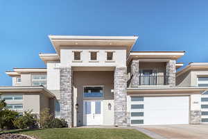 View of front facade featuring stone siding, stucco siding, a balcony, concrete driveway, and a garage