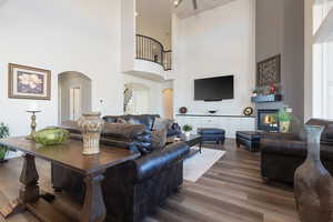 Living area featuring arched walkways, a glass covered fireplace, dark wood-type flooring, and a towering ceiling