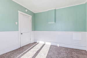 Unfurnished room featuring wood walls, wainscoting, carpet floors, and crown molding