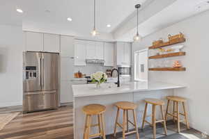 Kitchen featuring open shelves, appliances with stainless steel finishes, white cabinets, a kitchen bar, and light wood finished floors