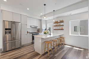 Kitchen with stainless steel appliances, open shelves, a breakfast bar area, white cabinets, and pendant lighting