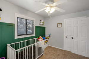 Bedroom featuring a crib, light carpet, and a ceiling fan