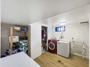 Washroom with light wood finished floors, a textured ceiling, washer and dryer, and wallpapered walls