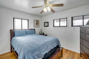 Bedroom with multiple windows, light wood-style flooring, ceiling fan, and a textured ceiling