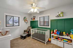 Carpeted bedroom featuring multiple windows, a crib, and ceiling fan