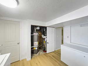 Finished below grade area featuring a textured ceiling, light wood-style floors, water heater, washer / clothes dryer, and heating unit