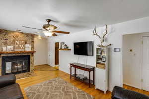 Living room with light wood finished floors, ceiling fan, a fireplace, and a textured ceiling