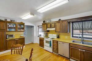 Kitchen featuring white range with electric cooktop, dishwashing machine, light countertops, light wood-style flooring, and a textured ceiling