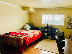 Bedroom with a textured ceiling, light wood finished floors, a textured wall, ornamental molding, and an office area