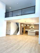 Unfurnished living room with recessed lighting, a towering ceiling, stairs, light wood finished floors, and a chandelier