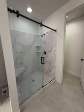 Primary full bath featuring a marble finish shower, light tile patterned floors, and recessed lighting
