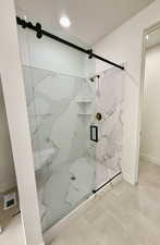 Primary sathroom with a marble finish shower and light tile patterned floors