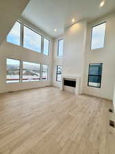Unfurnished living room featuring a high ceiling, a tile fireplace, recessed lighting, and light wood-style flooring