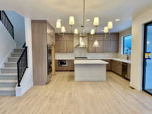 Kitchen with pendant lighting, a center island, light wood-type flooring, tasteful backsplash, and black appliances