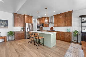 Kitchen with brown cabinetry, an island with sink, pendant lighting, a breakfast bar area, and appliances with stainless steel finishes