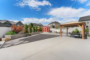 Fenced backyard with a patio area, a gazebo, a storage unit, outdoor dining space, and a residential view