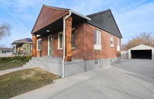 View of property exterior featuring a garage, an outdoor structure, covered porch, and brick siding
