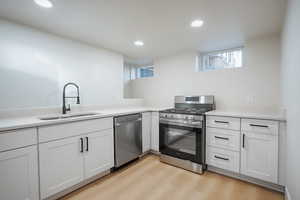 Kitchen featuring stainless steel appliances, white cabinetry, light wood-type flooring, recessed lighting, and light stone countertops