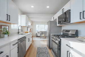 Kitchen with appliances with stainless steel finishes, white cabinetry, light wood-style flooring, light stone countertops, and recessed lighting