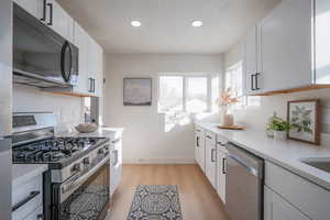 Kitchen with appliances with stainless steel finishes, light stone counters, white cabinetry, light wood finished floors, and recessed lighting