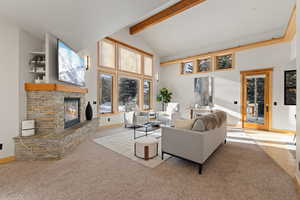 Living room featuring a stone fireplace, beam ceiling, high vaulted ceiling, and light colored carpet