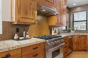 Kitchen featuring brown cabinets, stainless steel appliances, under cabinet range hood, and tasteful backsplash